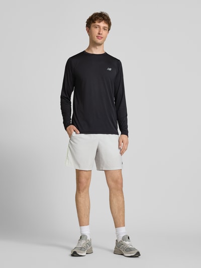Männermodel trägt Funktionsshirt mit Rundhalsausschnitt und Logo von New Balance, schwarz, Regular-Fit, Longsleeve, Rückenlänge 72 cm, Ganzkörperansicht von vorne.