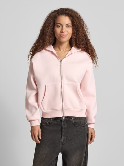 Modelka kobieca ma na sobie Relaxed Fit Sweatjacke mit Kapuze od REVIEW, różowa bawełna, logo, kieszenie, widok całej sylwetki z przodu.