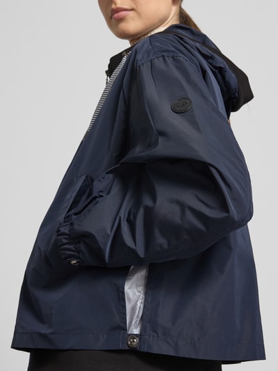 Modelka nosi Kurtka 'Jacke mit Zweiwege-Reißverschluss' von Gil Bret w kolorze granatowym z kapturem, wpuszczane kieszenie, krój relaxed fit, długość tyłu w rozmiarze 36: 59 cm, szerokość ramion: 52 cm, szerokość w rozmiarze 36: 57 cm, długość rękawów: 57 cm, zamek błyskawiczny dwustronny, detaliczne ujęcie na górną część tułowia z przodu.