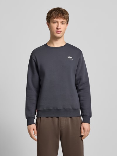 Männermodel trägt Sweatshirt mit gerippten Abschlüssen von Alpha Industries in Dunkelgrau, Baumwoll-Mix, lockerer Schnitt, Rundhalsausschnitt, Label-Details, Rückenlänge 67 cm, Ärmellänge 63 cm, Ganzkörperansicht von vorne.