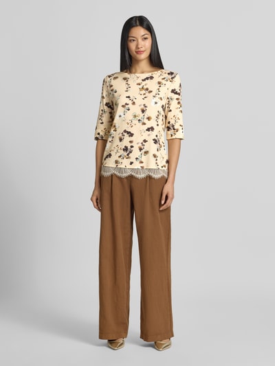 Frauenmodel trägt Regular Fit Bluse aus Baumwoll-Mix mit Spitzenbesatz von Marc Cain, floraler Allover-Print, 1/2-Arm, Ganzkörperansicht von vorne.