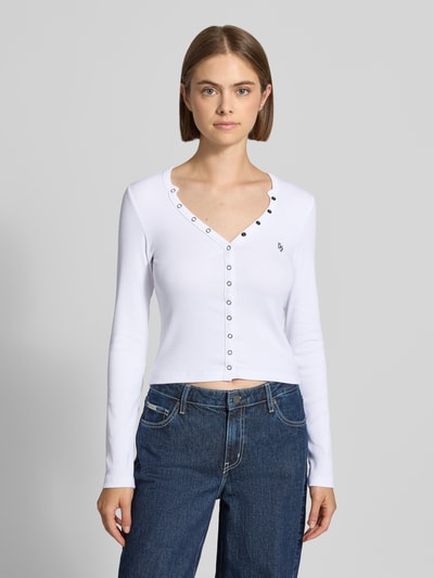 Frauenmodel trägt Slim Fit Longsleeve aus Baumwoll-Mix von GUESS in Weiß mit durchgehender Knopfleiste, Logo-Stitching, Ganzkörperansicht von vorne. Damen Longsleeve, elastischer Baumwoll-Mix, Rückenlänge Größe S 44 cm.