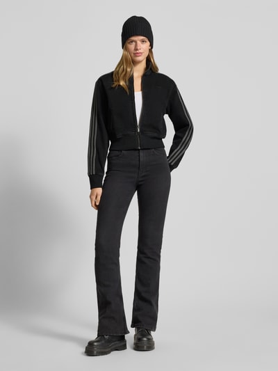 Frauenmodel trägt Jacke mit Reißverschluss von adidas Originals, schwarz, Regular-Fit, Cropped, Gerippte-Abschlüsse, Stehkragen, Label-Stitching, Eingrifftaschen, Ganzkörperansicht von vorne.