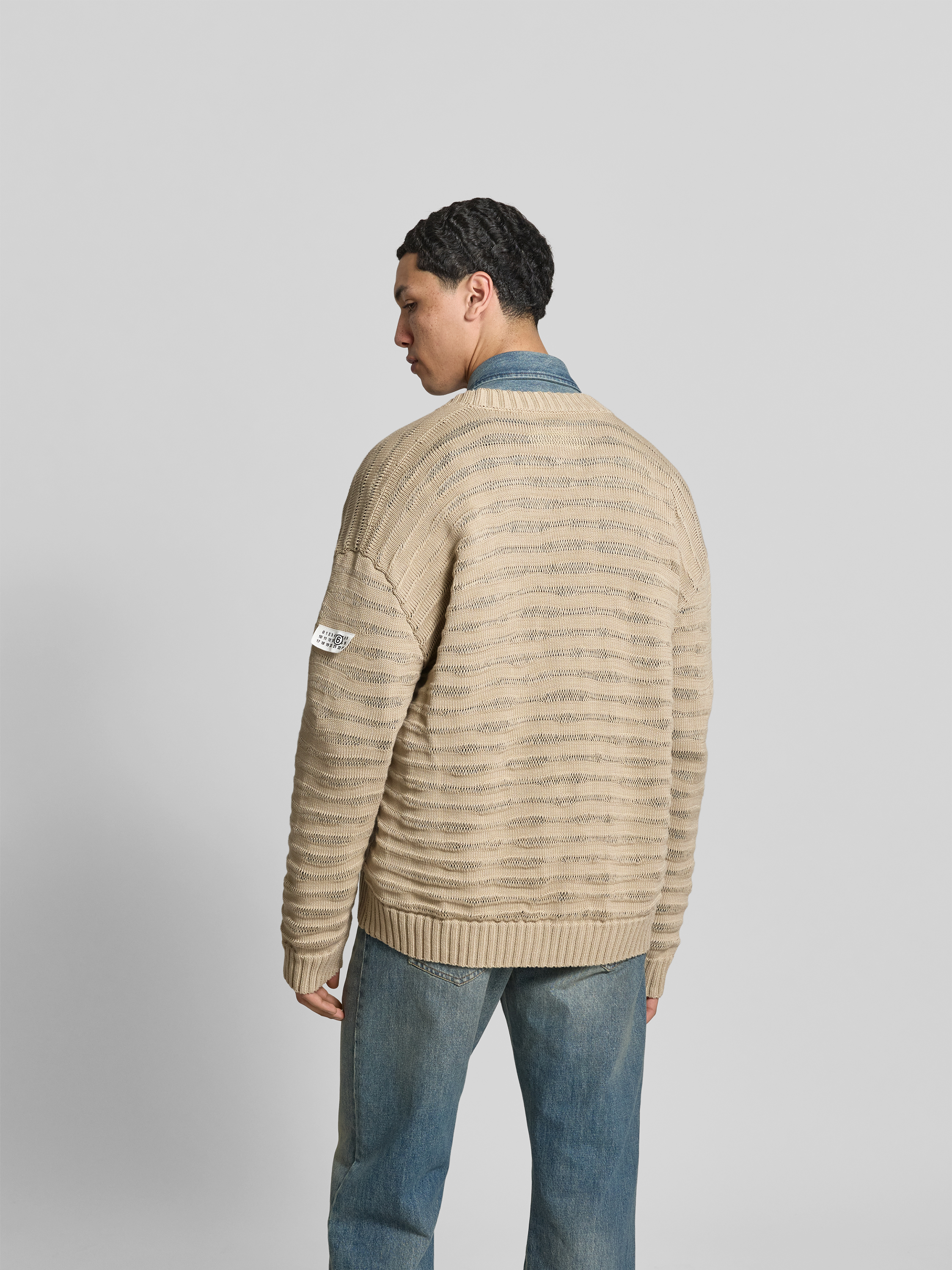 Männermodel trägt Relaxed Fit Cardigan in Strick-Optik von MM6 Maison Margiela aus reiner Baumwolle, beige, Ganzkörperansicht Rückansicht.