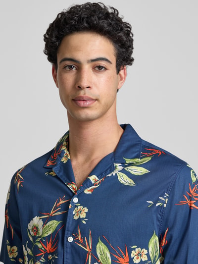Männermodel trägt Regular Fit Freizeithemd mit Reverskragen von Superdry in Dunkelblau mit floralem Muster aus Reiner Baumwolle, Nahaufnahme Oberkörper. Rückenlänge bei Größe M: 66 cm, Schulterbreite: 41 cm, Ärmellänge: 18 cm, Knopfleiste, Modern Fit.