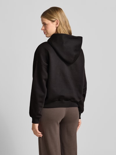 Frauenmodel trägt Hoodie mit Motiv-Stitching und Känguru-Tasche von REVIEW, Farbton Schwarz, Baumwoll-Mix, Regular-Fit, Ganzkörperansicht Rückansicht.