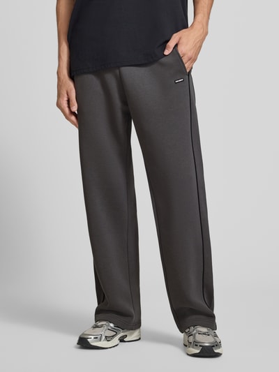 Männermodel trägt Straight Fit Sweatpants aus reiner Baumwolle mit Label-Patch von REVIEW, dunkles Grau, glatte Textur, Nahaufnahme Oberkörper, Herren Sweatpants von REVIEW, elastischer Bund, Eingrifftaschen, Innenbeinlänge bei Größe M 40 cm.