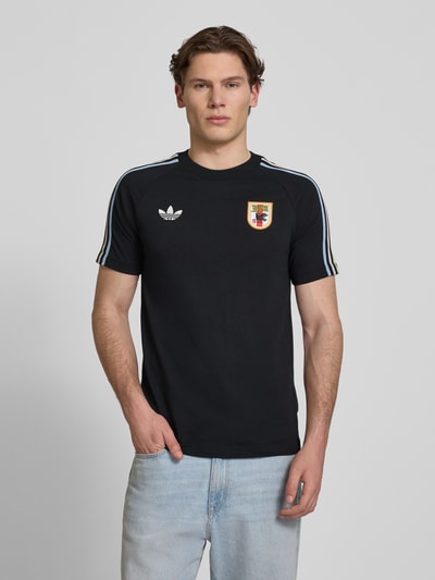 Männermodel trägt Regular Fit T-Shirt aus Baumwoll-Mix mit JFA-Applikation Modell 'NOIR' von adidas Originals, Optik: Unifarben, Logo-Stitching, Kontraststreifen, Rundhals, Kurzarm, Ganzkörperansicht von vorne.