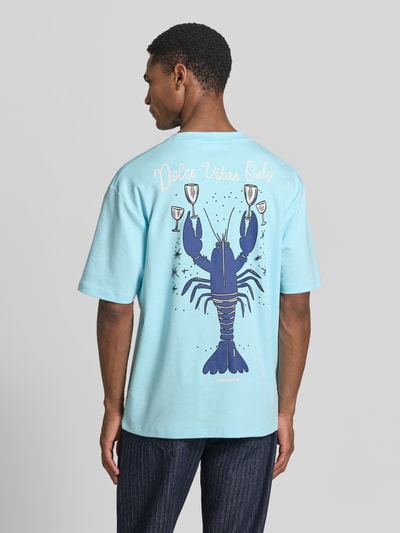Männermodel trägt Oversized T-Shirt mit Label-Print von Lindbergh in Hellblau aus Reine Baumwolle, Rückenlänge 70 cm, Ganzkörperansicht Rückansicht.