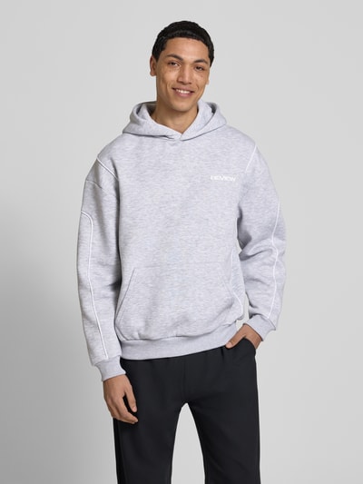 Männermodel trägt Hoodie mit Logo und Känguru-Tasche von REVIEW, hellgrau, Baumwoll-Mix, Regular-Fit, Ganzkörperansicht von vorne.