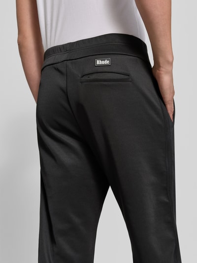 Männermodel trägt High Waist Sweathose mit Bundfalten von RHUDE in Schwarz, unifarben, strukturierte Jersey-Oberfläche, Rückansicht, Nahaufnahme Oberschenkel.