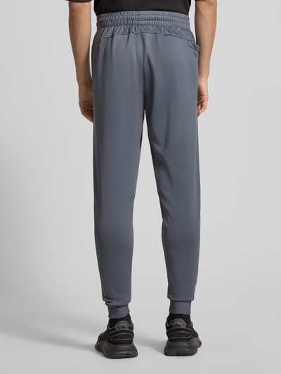 Męski model nosi Sweatpants mit elastischem Bund od Under Armour, szare, luźny krój, kieszenie, widok całej sylwetki z tyłu.