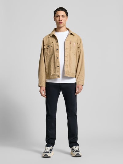 Męski model nosi Schmale Chino mit gerader Silhouette und mittlerer Bundhöhe od REVIEW, bawełna z domieszką elastanu, krój slim fit, średni stan, kieszenie z tyłu, szerokość w rozmiarze M: 43 cm, długość nogawki od wewnątrz w rozmiarze M: 81 cm, czarne spodnie, proste formy, gładka tekstura, pełny widok z przodu