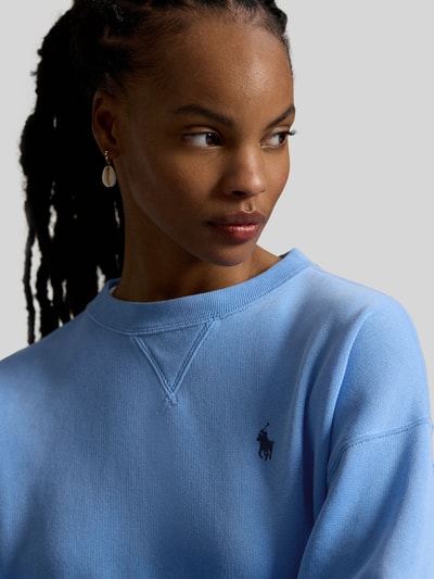 Vrouwenmodel draagt Regular Fit Sweatshirt aus Baumwoll-Mix van Polo Ralph Lauren in effen lichtblauw met logo-detail, sweatstof, ribboorden, crew neck, lange mouw, materiaal katoenmix. Close-up bovenlichaam.