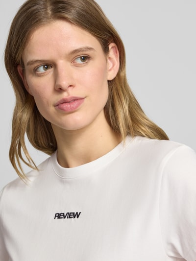 Frauenmodel trägt T-Shirt mit Rundhalsausschnitt und Logo-Stitching von Review, Baumwoll-Mix mit Stretch-Anteil, Nahaufnahme Oberkörper.