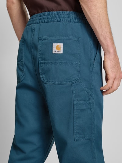Männermodel trägt Hose mit elastischem Bund Modell 'FLINT' von Carhartt Work In Progress aus Baumwolle in Blau, Detailaufnahme Rückansicht.