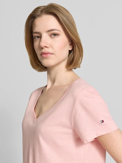 Frauenmodel trägt Regular Fit T-Shirt aus Baumwoll-Leinen-Mix von Tommy Hilfiger in zartem Rosa, Logo-Stitching, Melange-Optik, V-Ausschnitt, Kurzarm, Nahaufnahme Oberkörper.
