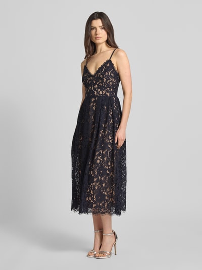 Modelka nosi knielanges Cocktailkleid mit Spitze und Spaghettiträgern od Jake*s Cocktail z mieszanki bawełny, taliowany fason, długość do kolan, koronka, podwójne cienkie ramiączka, dekolt w serek, zapięcie na haftkę i zamek błyskawiczny z tyłu, halka pod sukienkę, długość tyłu w rozmiarze 36: 123 cm, szerokość w rozmiarze 36: 34 cm, ciemny kolor, ażurowa tekstura, widoczne detale koronki, całkowity widok z przodu.