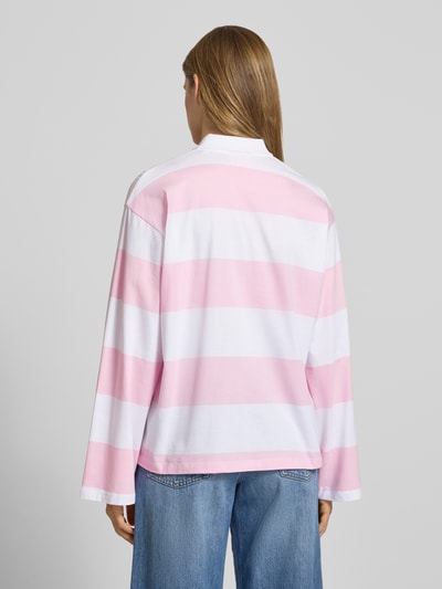 Frauenmodel trägt Relaxed Fit Poloshirt aus reiner Baumwolle Modell 'VILMA' von JJXX mit rosa-weißen Blockstreifen, langärmelig, Rückenlänge 62 cm, Ganzkörperansicht Rückansicht.
