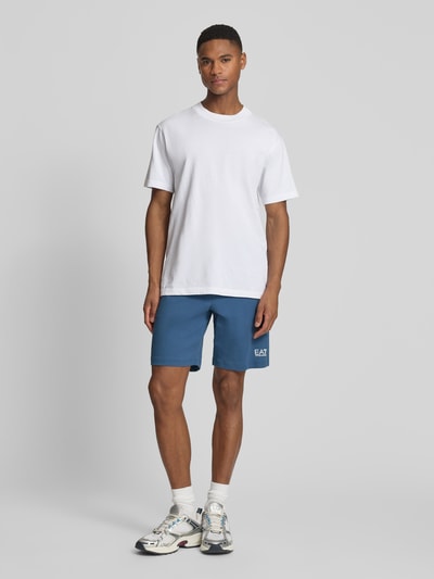 Männermodel trägt Sweatshorts mit Logo und Eingrifftaschen von EA7 Emporio Armani aus reiner Baumwolle, Regular-Fit, Ganzkörperansicht von vorne.