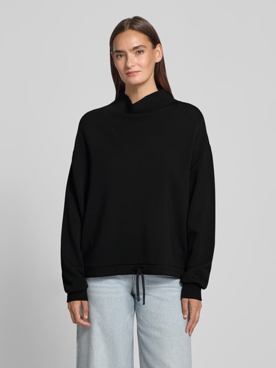 Kobieta nosi Regular Fit Sweatshirt aus Viskose-Mix Modell 'Betsy' od VARLEY, czarna mieszanka wiskozy, stójka, tunel w pasie, krój regular fit, widok całej sylwetki z przodu.