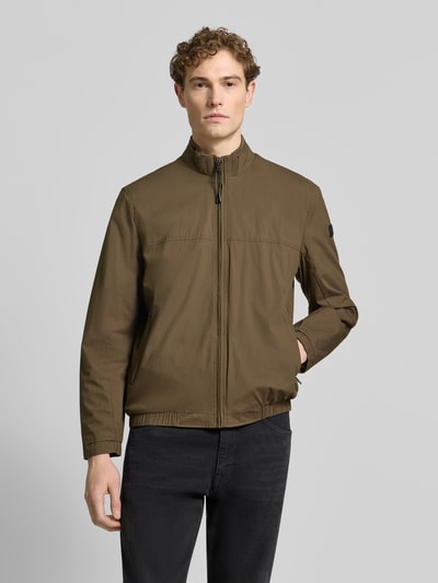 Männermodel trägt Jacke mit Stehkragen Modell 'Calvin' von Brax in Oliv, Baumwoll-Mix mit Stretch, Reißverschluss, Ganzkörperansicht von vorne.