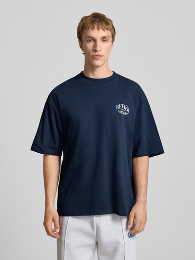 Männermodel trägt T-Shirt mit Label-Detail von REVIEW, dunkelblau, Reine Baumwolle, Lockerer-Schnitt, Rundhalsausschnitt, 1/2-Arm, Rückenlänge bei Größe M 68 cm, Ganzkörperansicht von vorne.