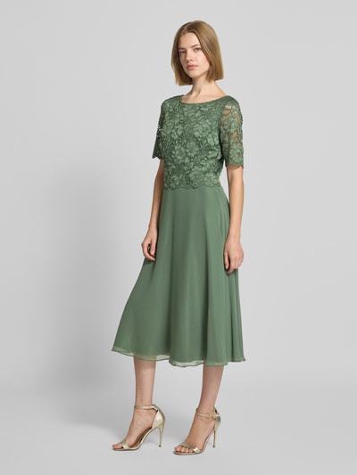 Frauenmodel trägt Tailliertes Cocktailkleid mit Spitzenbesatz von Vera Mont in Grün mit floralen Strukturen, Ganzkörperansicht von vorne.