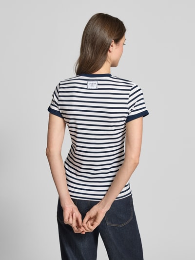 Frauenmodel trägt Guess T-Shirt mit Rundhalsausschnitt und Label-Print, gestreift in Dunkelblau-Weiß, Material-Mix, körpernah, Ganzkörperansicht Rückansicht.