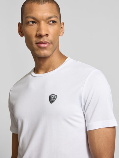 Männermodel trägt T-Shirt aus Viskose-Mix mit Label-Patch von EA7 Emporio Armani, Slim-Fit, Rundhalsausschnitt, Nahaufnahme Oberkörper.