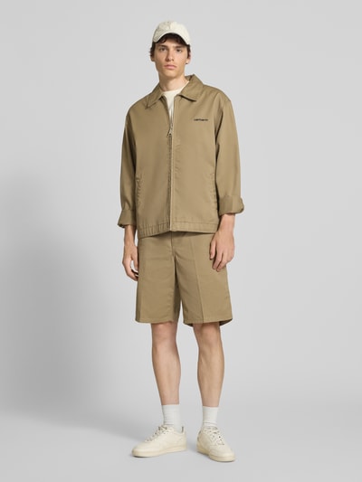 Männermodel trägt Bermudas mit Gesäßtaschen von Carhartt Work In Progress im Material-Mix mit Baumwoll-Anteil, Regular-Fit, Eingrifftaschen, Farbe Sand, Bundweite 45 cm, Innenbeinlänge 26 cm, Ganzkörperansicht von vorne.