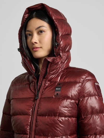 Frauenmodel trägt Jacke in Stepp-Optik Modell 'CAROLL' von Blauer USA in glänzendem Dunkelrot, Logo-Detail, Nahaufnahme Oberkörper.