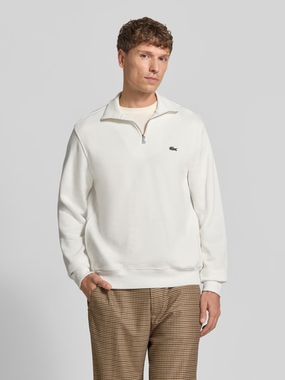 Männermodel trägt Regular Fit Troyer aus reiner Baumwolle von Lacoste in Weiß mit feiner Struktur, Ganzkörperansicht von vorne. Herren Troyer von Lacoste.