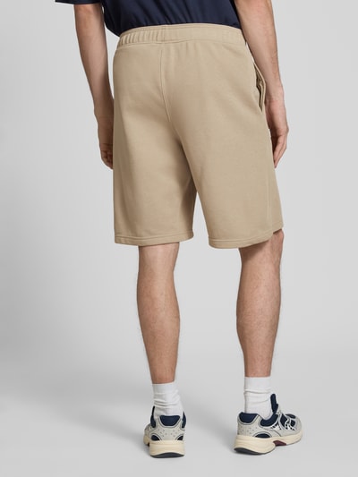 Männermodel trägt Bermudas mit elastischem Bund und Label-Stitching von CHAMPION in Beige, Baumwoll-Mix, Längsnähte, Ganzkörperansicht Rückansicht.