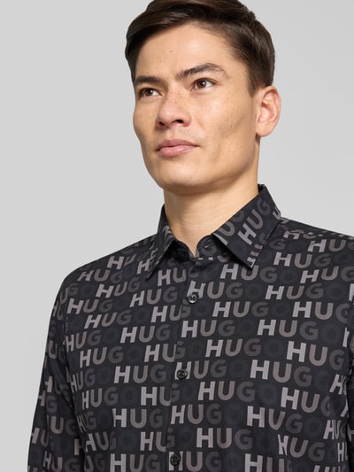 Männermodel trägt Slim Fit Freizeithemd aus reiner Baumwolle Modell 'ERMO' von HUGO mit Allover-Muster in Schwarz, Nahaufnahme Oberkörper.
