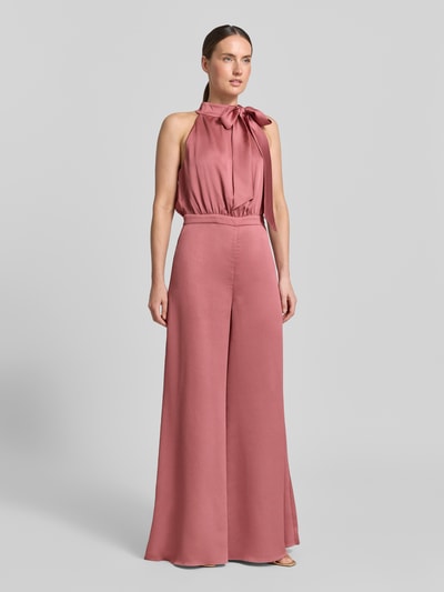 Vrouwenmodel draagt Jumpsuit mit Schluppe und rückseitigem Knopfverschluss van Swing in oudroze satijn met aangesloten fit, detail strik en knoopsluiting achter, materiaal glad met lichte glans, volledige lichaamsvooraanzicht.