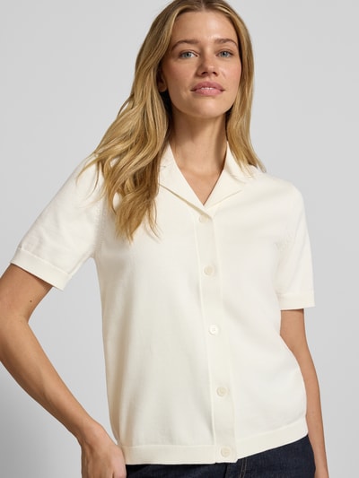 Modelka kobieca nosi Regular Fit Poloshirt aus reiner Bio-Baumwolle Modell 'AMOUR' od Selected Femme, kremowy, krój regular fit, krótki rękaw, jednolity kolor, dzianina z bio-bawełny, kołnierzyk polo, zapięcie na guziki, nadruk z logo, widok na górną część ciała z przodu.