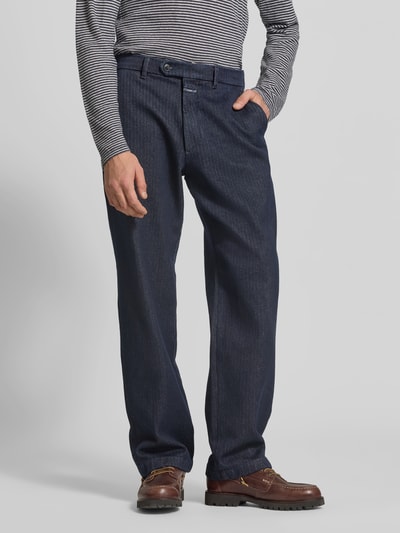 Męski model nosi Relaxed Fit Hose aus reiner Baumwolle od Closed, granatowy, szerokie nogawki, kieszenie, bawełniana tkanina, Szerokość w rozmiarze 32/32: 43 cm, długość wewnętrzna nogawki: 80 cm, patch z logo, zapięcie na guzik i zamek, widok całej sylwetki z przodu.