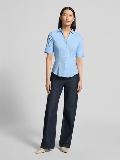 Frauenmodel trägt Hemdbluse im Halbarm-Design von More & More in Hellblau, taillierte Passform, Baumwoll-Mix, Hemdblusenkragen, Knopfleiste, Ganzkörperansicht von vorne. Rückenlänge bei Größe 36: 65 cm, Ärmellänge: 28 cm.