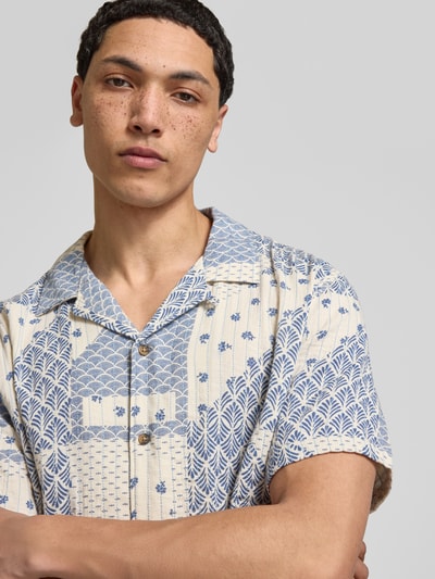 Męski model nosi Relaxed Fit Freizeithemd aus reiner Baumwolle Modell 'PISARROT' od Pepe Jeans w jasnobeżowym kolorze z niebieskim, geometrycznym wzorem patchwork, materiał bawełniany, krótkie rękawy, widoczna listwa guzikowa, wzór allover, label-application, krój relaxed fit, perspektywa: zbliżenie na górną część ciała z przodu.