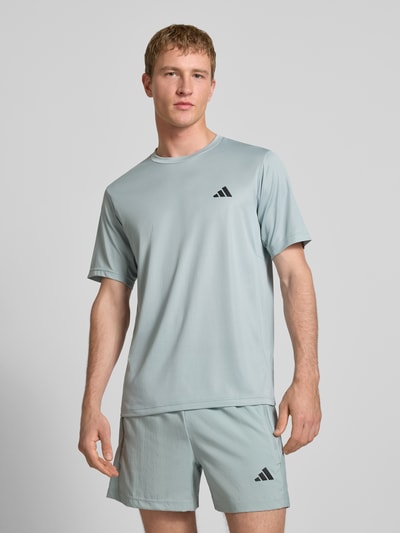 Männermodel trägt T-Shirt mit Logo und Rundhalsausschnitt von adidas Training in Hellgrau, glatte Textur, Regular Fit, Ganzkörperansicht von vorne.