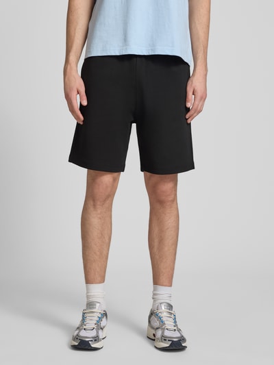 Männermodel trägt Shorts mit Label-Stitching mit elastischem Bund von CHAMPION, schwarz, Baumwoll-Mix, Ganzkörperansicht von vorne.