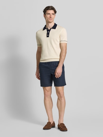 Männermodel trägt Slim Fit Poloshirt mit Logo-Stitching von Gant in Beige und Dunkelblau, Baumwoll-Modal-Mix, Ganzkörperansicht von vorne.