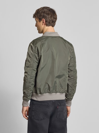 Männermodel trägt Regular Fit Bomberjacke mit Logo-Patch von Alpha Industries in Olivgrün mit Eingrifftaschen und Stehkragen, Ganzkörperansicht Rückansicht
