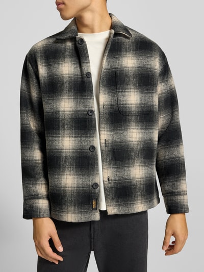 Männermodel trägt Regular Fit Hemdjacke mit Brusttasche Modell 'SOHO OLLIE' von JACK & JONES, kariert in Schwarz-Beige, Nahaufnahme Oberkörper. Kontext: Herren Hemdjacke mit Kentkragen, durchgehender Knopfleiste, Rückenlänge 71 cm, Schulterbreite 41 cm, Ärmellänge 65 cm.