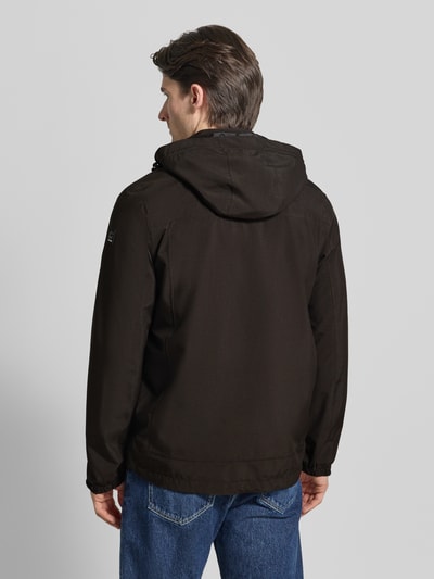 Męski model nosi Jacke mit Napoleontasche Modell 'KOS' od Killtec, czarna, kaptur z tunelem, krój regular fit, widok całej sylwetki od tyłu.