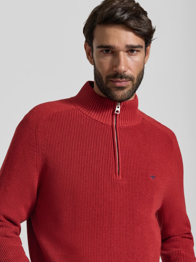 Męski model nosi Regular Fit Strickpullover aus reiner Baumwolle mit Troyer-Kragen od Fynch-Hatton, krój regular fit, kolor czerwony, prążkowana struktura, wyhaftowane logo, krój z długim rękawem, prążkowane wykończenia, imitacja dzianiny, Długość tyłu w rozmiarze M: 65 cm, Długość rękawów w rozmiarze M: 75 cm, zbliżenie na górną część tułowia.