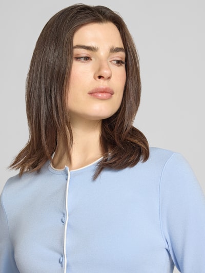 Frauenmodel trägt Strickjacke aus Viskose-Mix Modell 'COLLECTIONS' von Marc Cain in Hellblau mit glatter Textur, Nahaufnahme Oberkörper. Taillierte Passform, durchgehende Knopfleiste.
