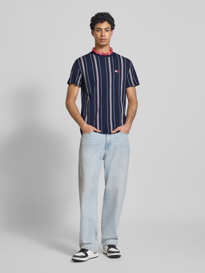 Männermodel trägt Regular Fit T-Shirt aus reiner Baumwolle von Tommy Jeans, Optik:Allover-Muster, Rundhals, Kurzarm, Label-Stitching-Applikation, Ganzkörperansicht von vorne.
