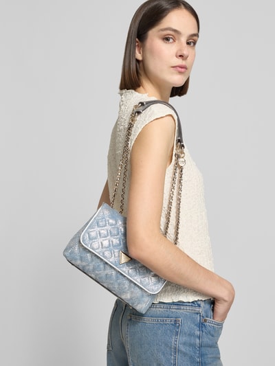 Frauenmodel trägt Shoulder Bag in Stepp-Optik Modell 'GIULLY' von Guess, Ketten-Optik, Logo-Detail, Magnetverschluss, Ganzkörperansicht von vorne.